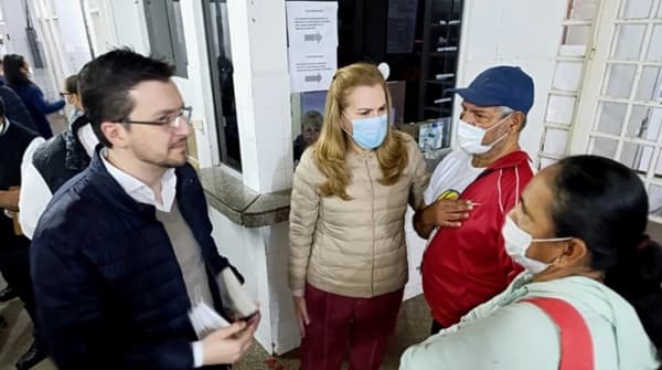 La ministra de Salud María Teresa Barán, vestida con campera beige y barbijo azul, conversa con personal médico y funcionarios durante su visita de inspección al Hospital General de Lambaré. En la imagen se observa al viceministro Saúl Recalde con anteojos y saco azul marino, junto a profesionales de la salud con uniformes y barbijos en los pasillos del centro hospitalario.