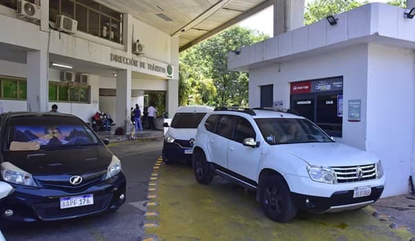 Vehículos estacionados frente a la Dirección de Tránsito de Asunción, mientras ciudadanos realizan gestiones administrativas en el lugar, en una jornada con alta concurrencia.
